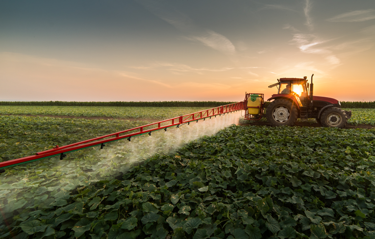 Green agricultural sprayer applying fertilizer in crop field at sunset — diesel engine optimization with AgroEcoPower.